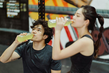 Zwei Menschen trinken nach dem Sport aus einer Flasche